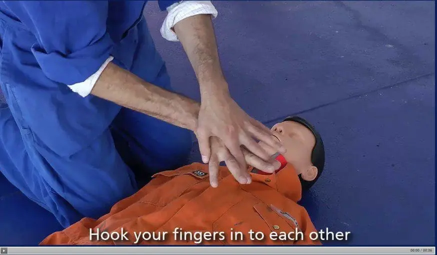 First aid instructor demonstrating finger hook technique for recovery position on casualty wearing orange shirt during Basic First Aid training
