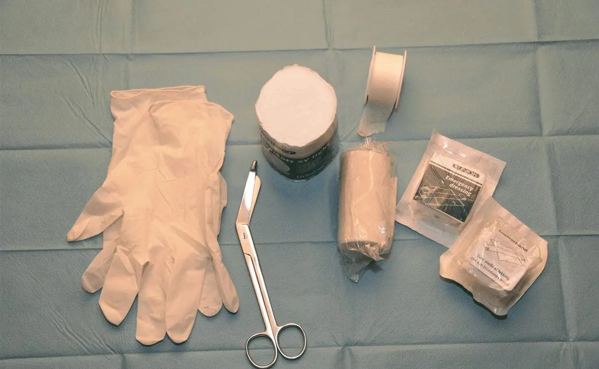 Medical first aid kit contents including sterile gloves, scissors, gauze, tape, antiseptic solution, and bandages arranged on blue surface for STCW Basic First Aid training