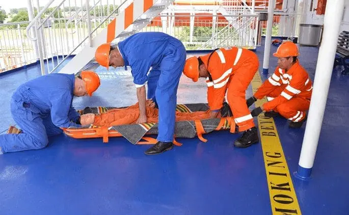 Maritime first aid training demonstration with emergency responders practicing casualty evacuation procedures on industrial platform using stretcher and safety equipment