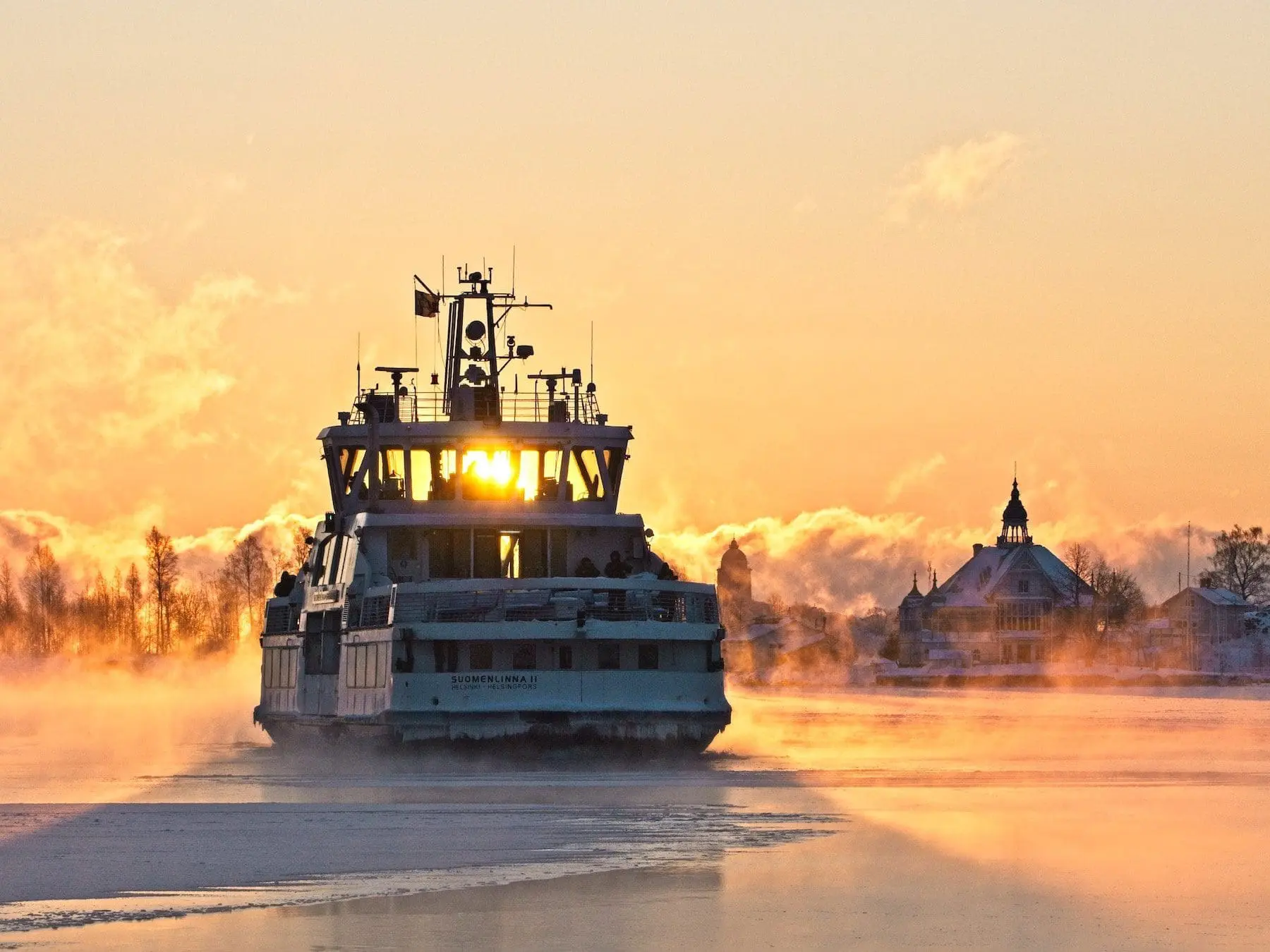 Industrial ferry ship Suomenlinna II navigating frozen river at sunrise with misty atmosphere and church spire visible on shore