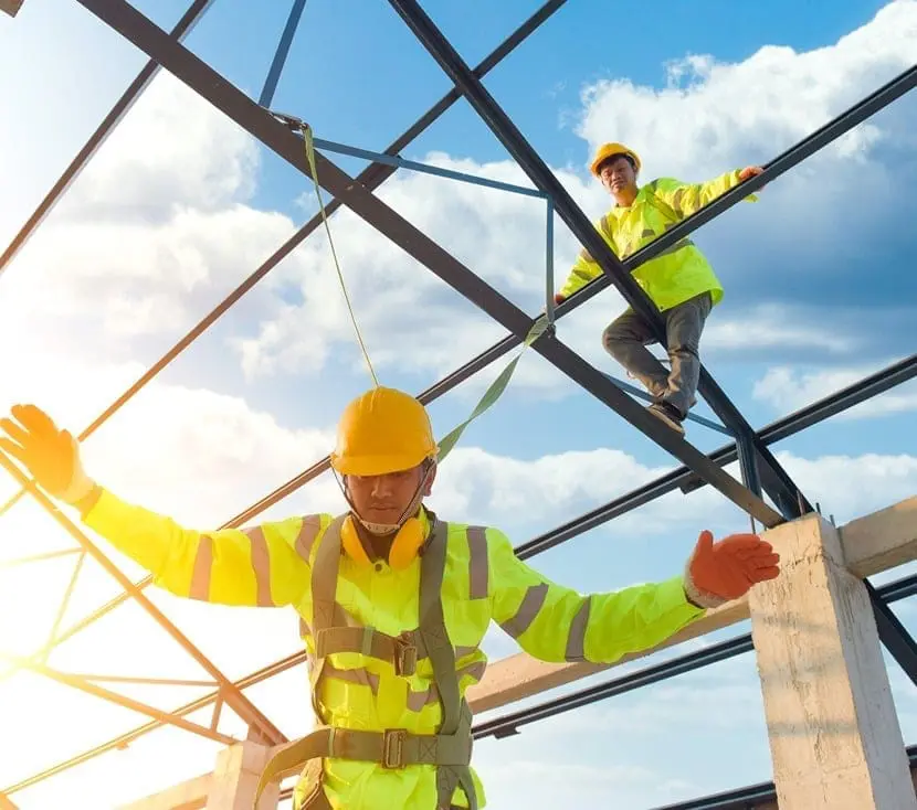Two construction workers in high-visibility gear and hard hats working on steel framework at height, demonstrating safe working practices and fall protection equipment