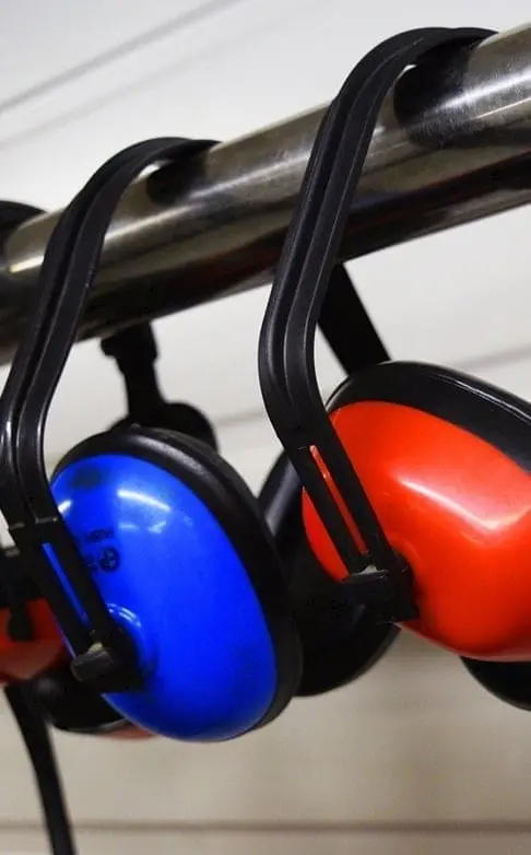 Two colorful ear defenders with blue and red earcups hanging on a metal bar, representing noise protection equipment for workplace safety training