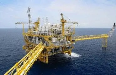 Large offshore oil and gas platform with yellow structural components and drilling equipment in deep blue ocean water