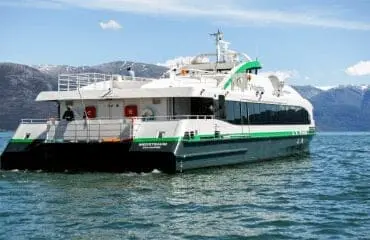 Green and white passenger ferry boat on blue water with mountains in background, representing maritime training and STCW certification courses