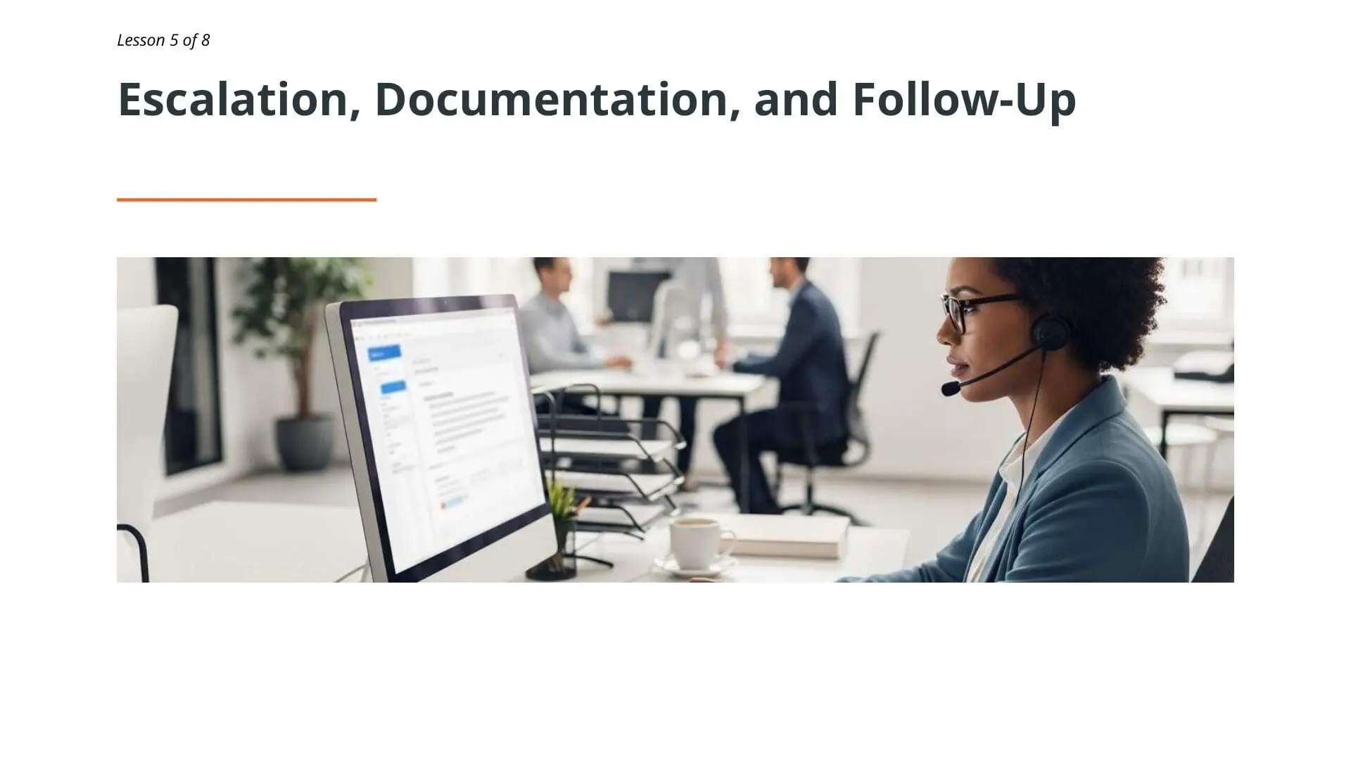 Customer service representative wearing headset at desk reviewing complaint documentation on computer monitor in professional office environment