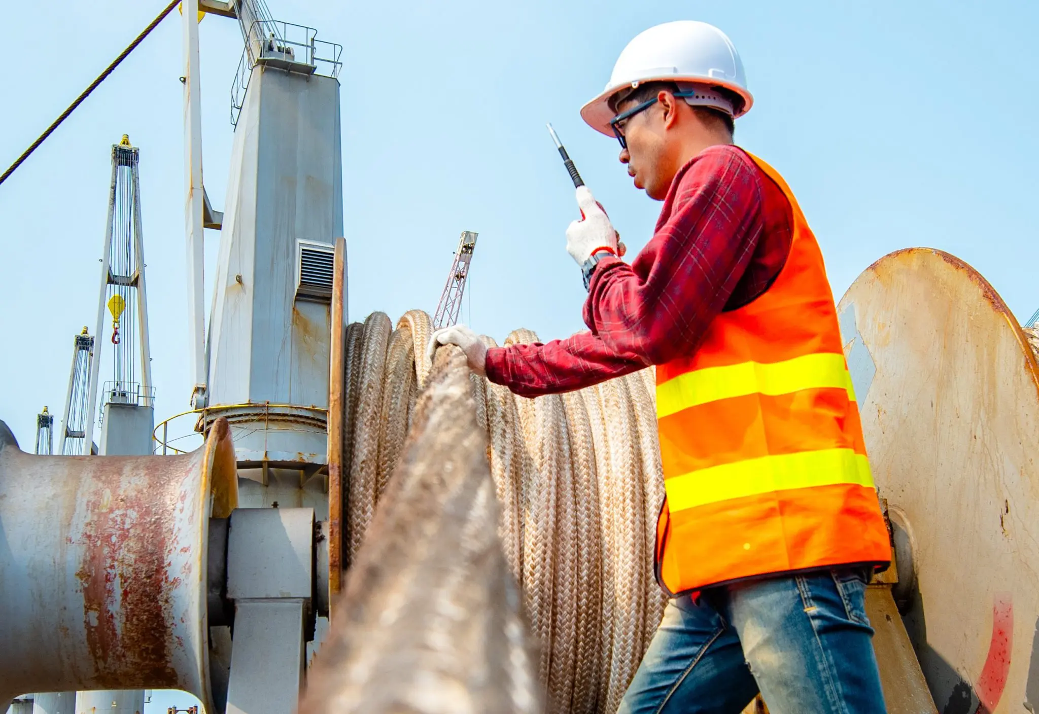 Construction worker in safety gear inspecting marine rigging ropes on industrial vessel, demonstrating ship safety officer inspection duties