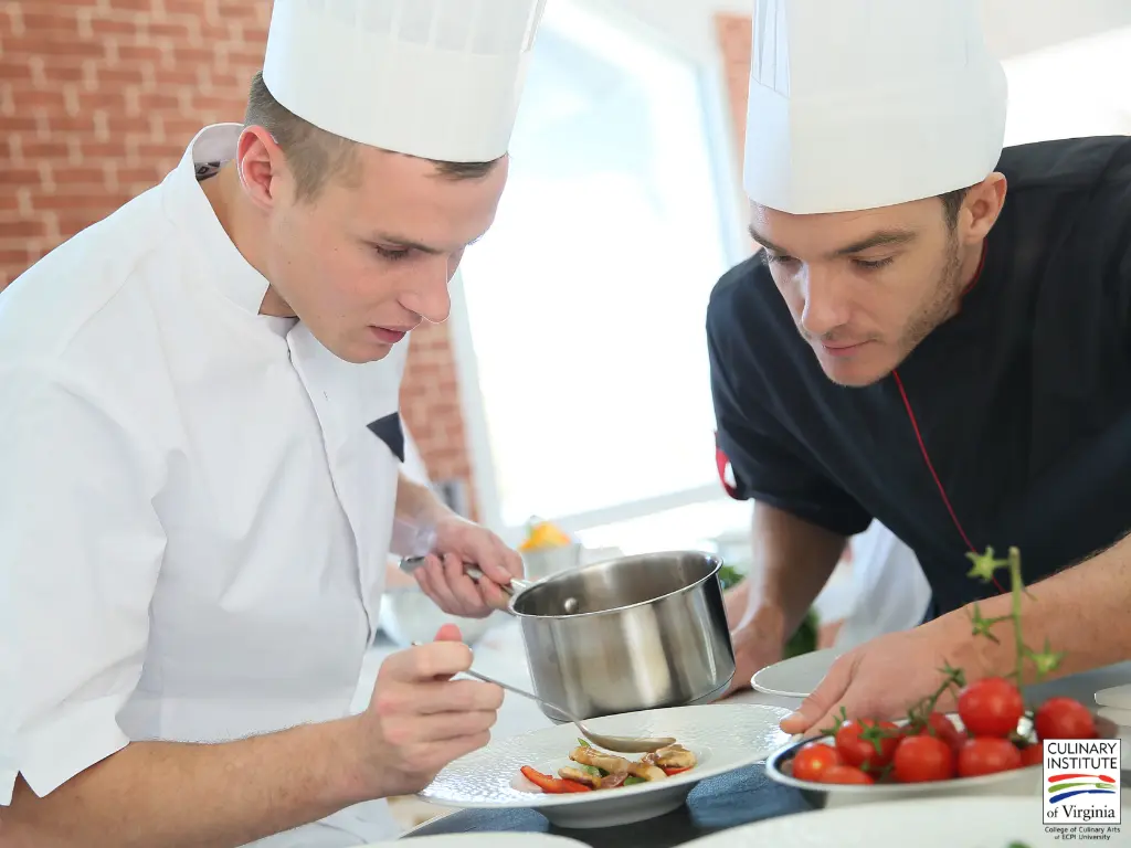 Two chefs in white and black chef coats and hats preparing food in a professional kitchen setting, demonstrating HACCP food safety practices with fresh vegetables and cooking equipment